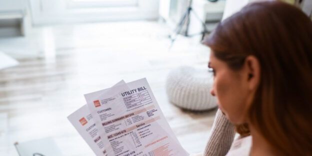 Indoor shot of casually dressed young woman holding papers in her hands, calculating family budget, trying to save some money , having stressed and concentrated look.