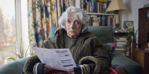 An elderly woman seated in a chair, clutching a document.