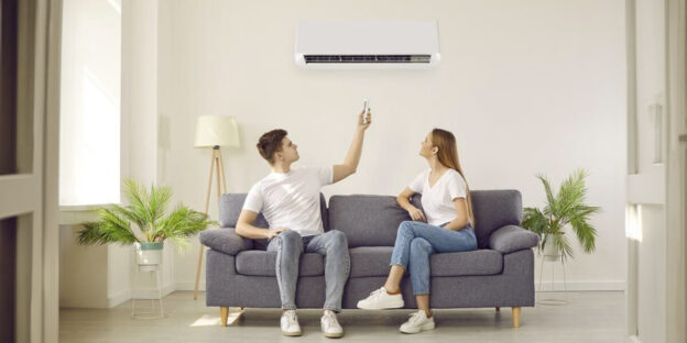 A couple sitting on a couch in front of a wall-mounted air conditioner.
