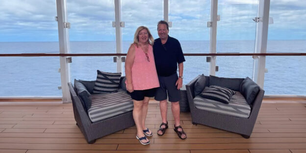 A couple enjoying the view on a cruise ship's deck, with the vast ocean stretching out behind them.
