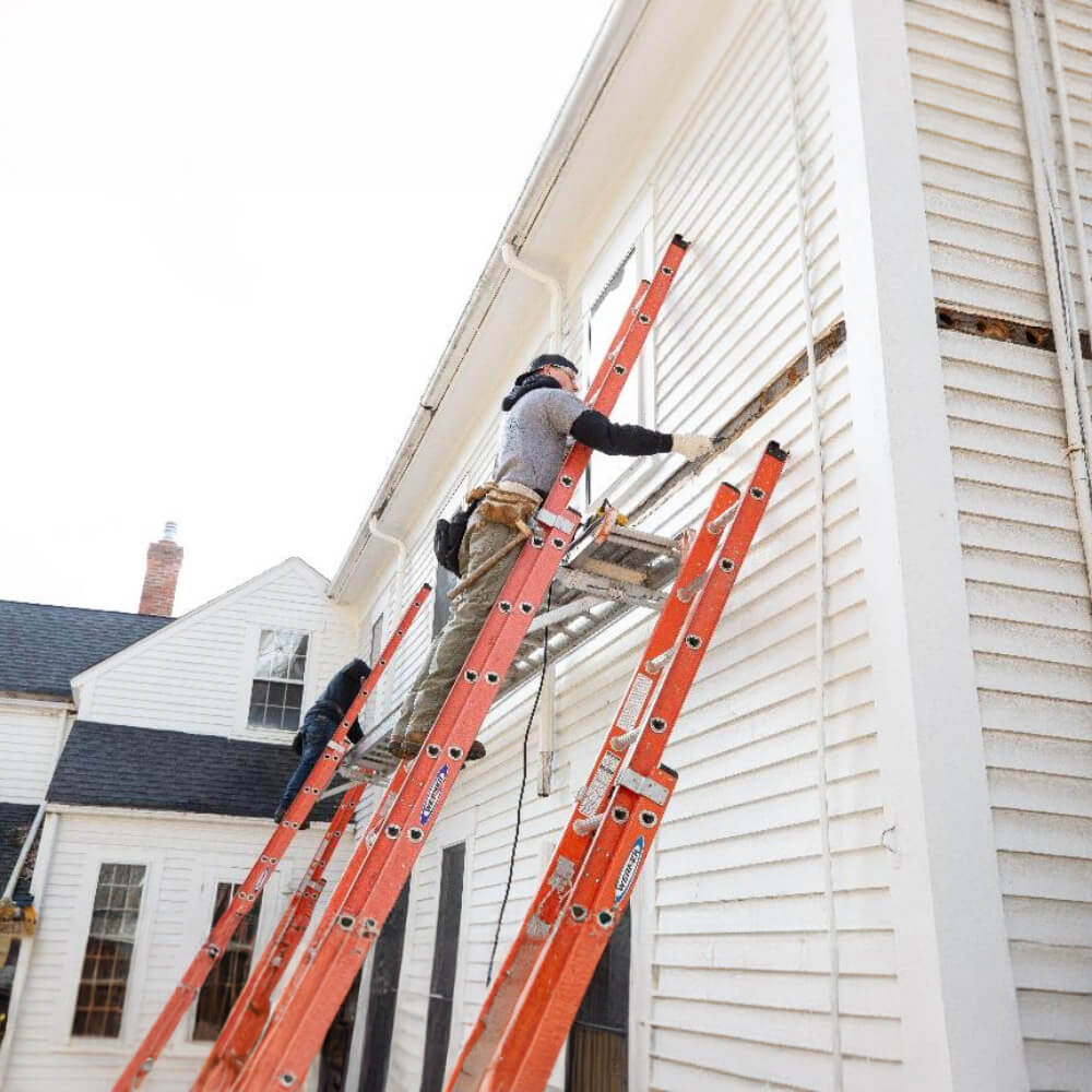 Two construction workers on ladders renovating a house.