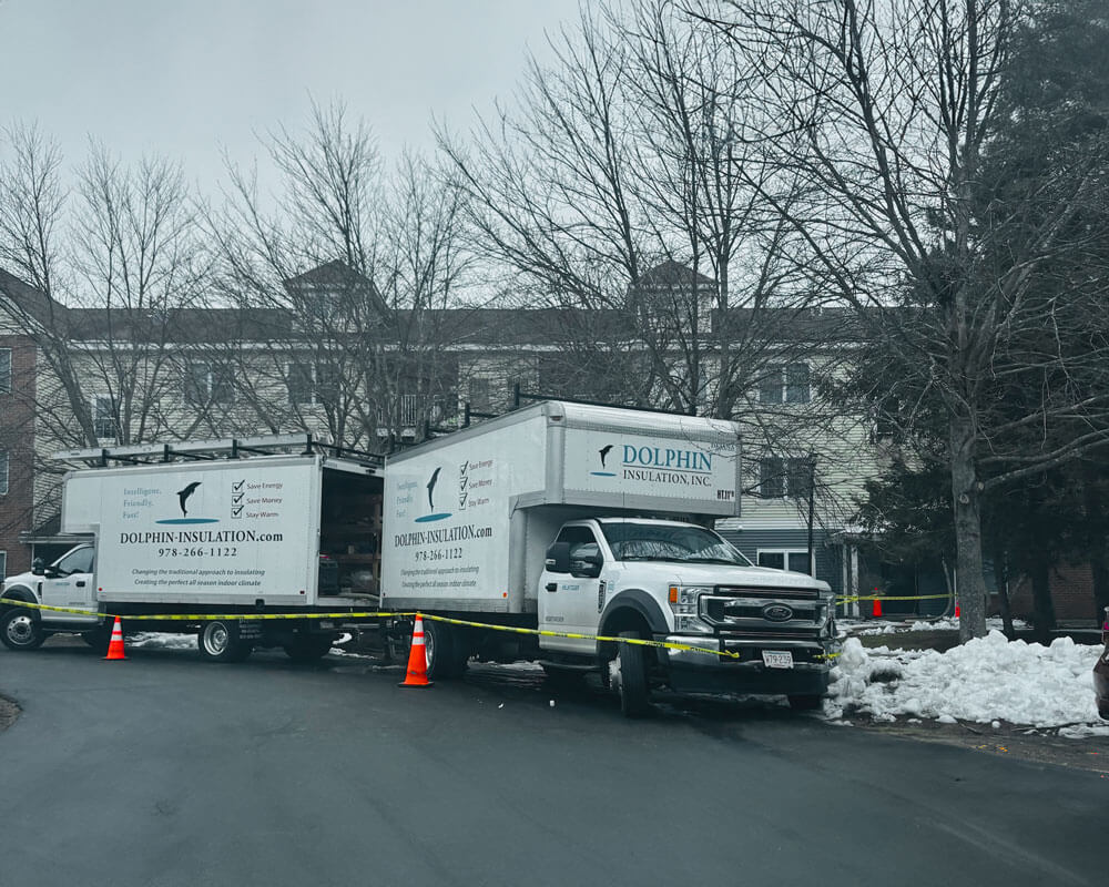 Two Dolphin Insulation trucks parked outside a building, with caution tape and traffic cones indicating an active worksite.