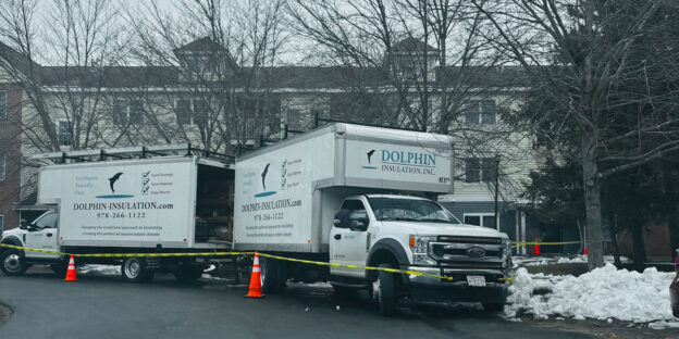 Two Dolphin Insulation trucks parked outside a building, with caution tape and traffic cones indicating an active worksite.