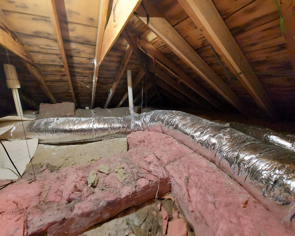 A dusty attic with exposed insulation and HVAC ductwork running across the floor.