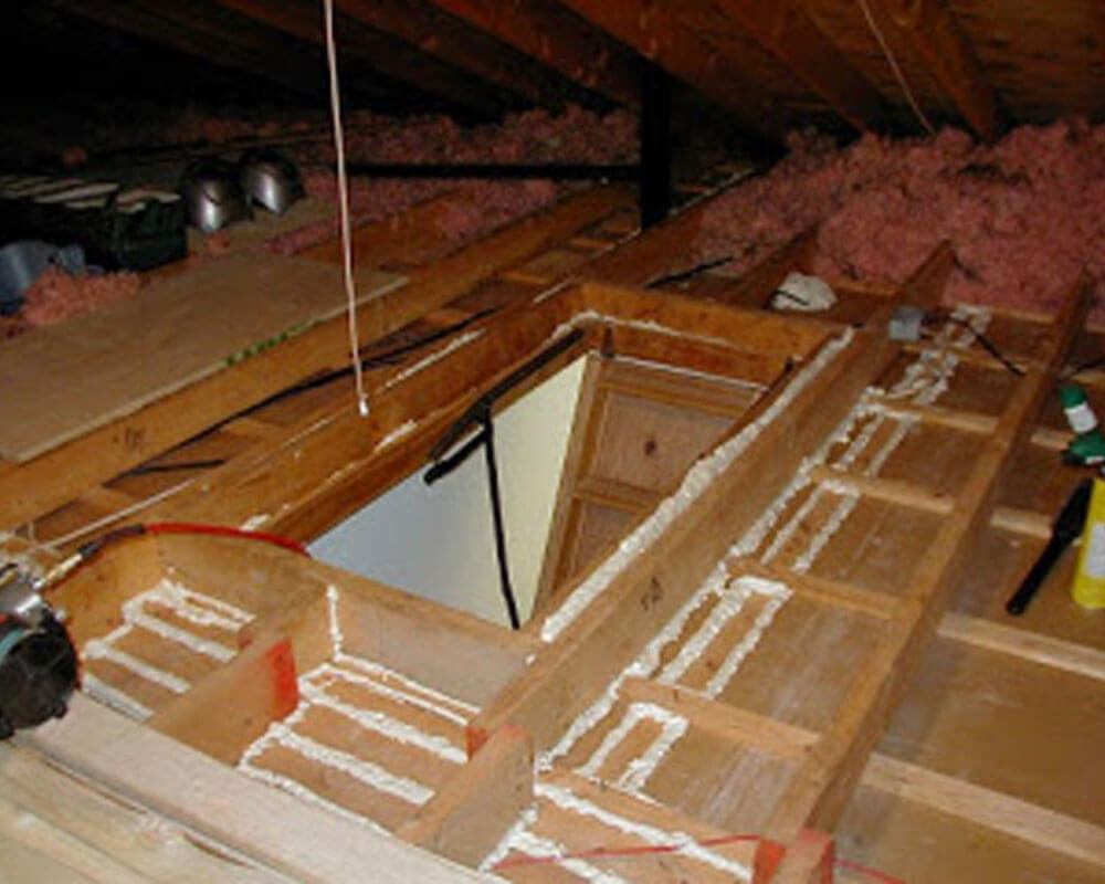 An attic undergoing insulation work, with foam sealing applied around exposed framing.