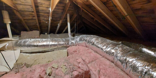 A dusty attic with exposed insulation and HVAC ductwork running across the floor.